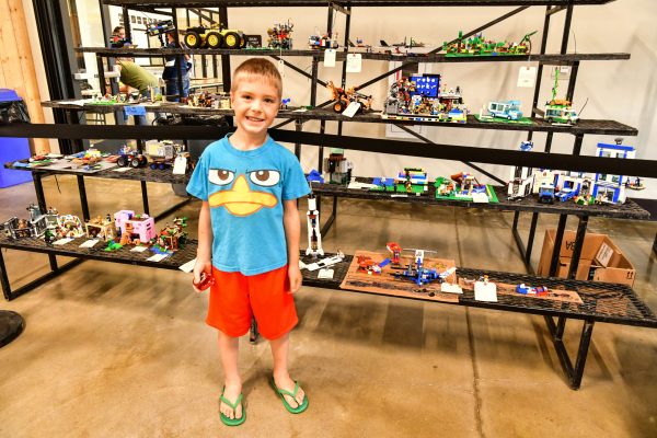 boy standing proudly with his lego creation at fair